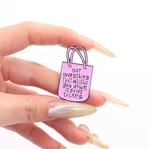 Gros plan d'une broche en émail rose en forme de sac avec texte inspirant tenue