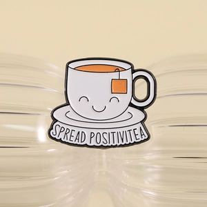 Close-up of smiley teacup enamel pin featuring SPREAD POSITIVITEA funny pun text