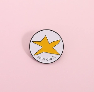 Détail d'un pin's rond en émail blanc avec étoile jaune et texte humoristique