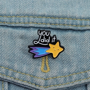 Detail of 'YOU did it' enamel star brooch pinned on a light blue denim jacket pocket