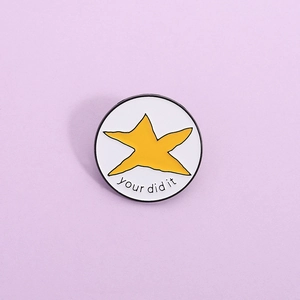 Détail d'un pin's en émail blanc avec étoile jaune et texte your did it gravé