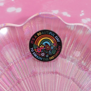 Detail of colorful floral enamel badge with feminist slogan in iridescent shell tray