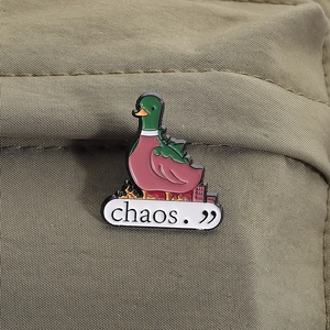 Detail of creative green duck enamel pin with chaos text on olive green fabric background