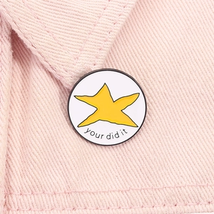 Détail macro d'une broche étoile en émail blanc avec texte You Did It sur denim rose