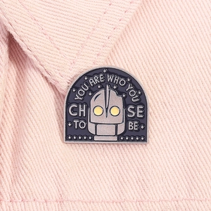Macro shot of Iron Giant enamel pin featuring the text You Are Who You Choose To Be