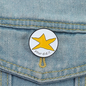 Détail macro d'une broche étoile en émail blanc avec texte 'you did it' sur denim