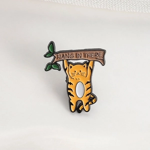 Détail d'un pin's en émail chat roux avec slogan Hang In There suspendu à une branche