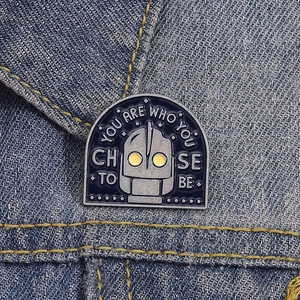 Enamel robot pin with Iron Giant design and quote on denim jacket background