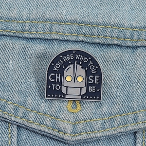 Macro shot of Iron Giant enamel pin with inspirational quote on denim fabric