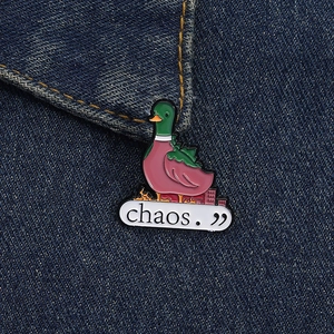 Detail of a green duck metal enamel pin with chaos text on denim jacket pocket