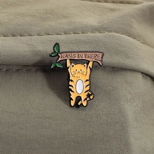 Broche en émail chat rayé avec texte HANG IN THERE sur un fond en tissu beige