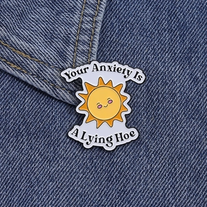Detalle del pin esmaltado de sol inspirador con texto humorístico sobre fondo de tela vaquera