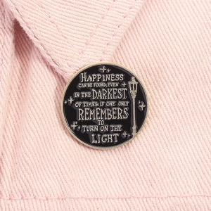 Macro view of round black enamel badge pin with gold quote on pink denim fabric