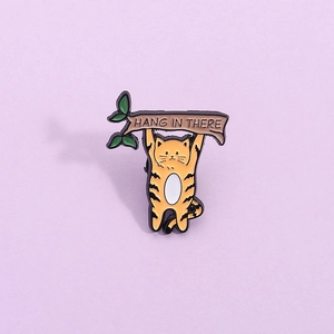 Gros plan sur un pin's émaillé avec chat sur une branche et texte Hang In There