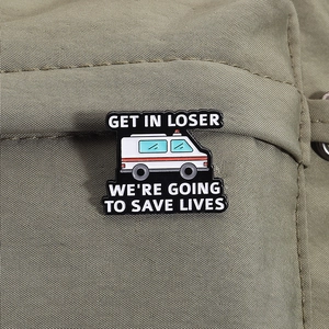 Macro shot of ambulance enamel pin with GET IN LOSER text on olive green fabric