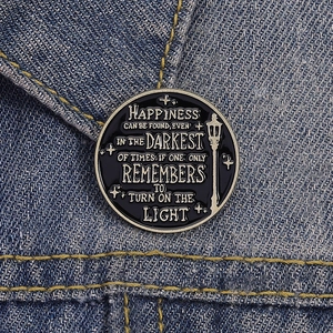 Detailed view of enamel wizard pin on denim jacket featuring gold inspirational text