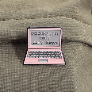 Pink laptop enamel pin with Document It Or It Didn't Happen text on brown fabric