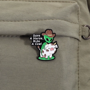 Detail of UFO alien riding a cow enamel pin with slogan on green canvas bag