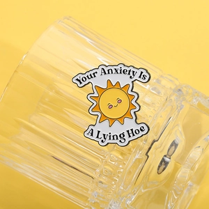 Detalle de pin esmaltado de sol amarillo con cita Your Anxiety Is A Lying Hoe
