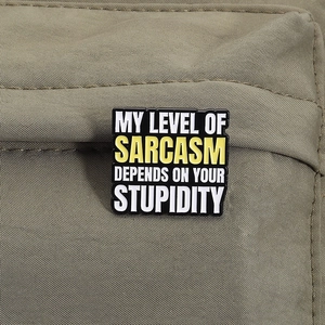 Detail view of square enamel brooch with sarcastic quote on a khaki canvas backpack