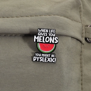 Detailed macro view of enamel watermelon pin with humorous quote on a canvas bag