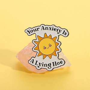 Detalle de pin esmaltado de sol sonriente con mensaje motivador sobre la ansiedad