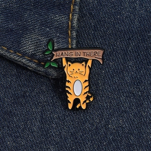 Détail macro du pin's chat orange émaillé sur jean avec texte Hang In There gravé