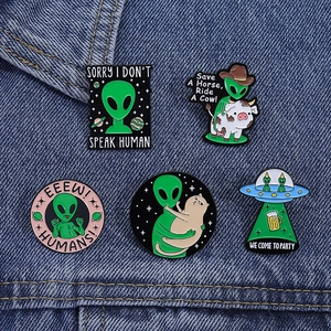 Detailed set of five green alien and space cat enamel pins on blue denim fabric
