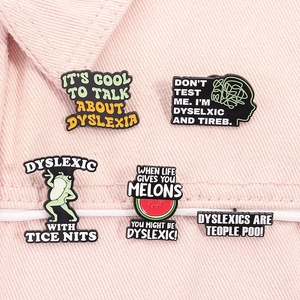 Detail view of five enamel pins with dyslexia themes on pink denim background