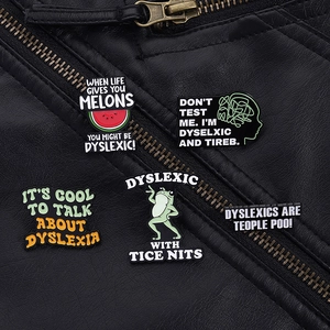 Close-up of dyslexia awareness enamel pins on a black leather jacket with brain and frog icons