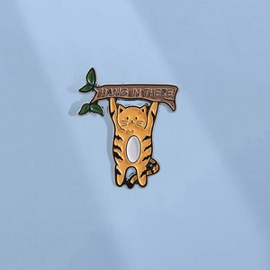 Détail du pin's émaillé chat orange sur une branche avec texte Hang In There