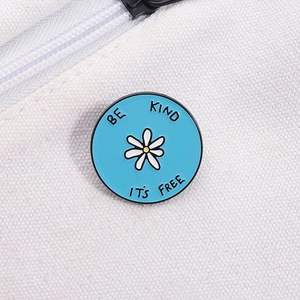 Détail d'une broche en émail bleu sur un sac en toile blanche avec texte Be Kind