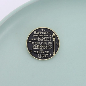 Detailed macro view of enamel pin with quote about finding light in the darkest of times