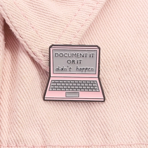Detailed view of pink laptop enamel pin on fabric with document text engraving