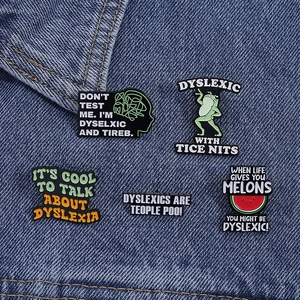 Detailed close-up of colorful dyslexia awareness enamel pins on blue denim fabric