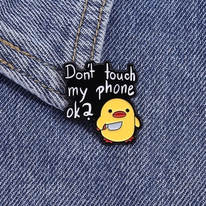 Detail of cute yellow duck enamel pin with a knife on denim fabric showing metal texture