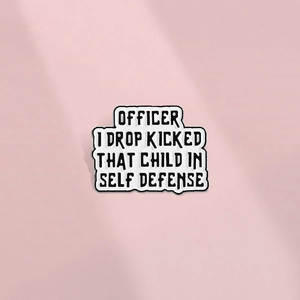 Detail of white enamel pin featuring black text Officer I Drop Kicked That Child in Self Defense