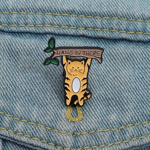 Broche en émail chat roux sur jean avec inscription Hang In There pour motivation