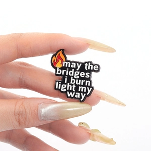 Emaille-Anstecknadel mit Flamme und dem Spruch 'may the bridges i burn light my way' Design