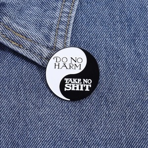 Macro d'un pin's Yin Yang en émail avec texte Do No Harm sur tissu denim bleu