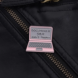 Detailed view of pink laptop enamel pin with creative quote on black leather jacket
