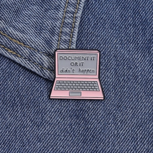 Detailed close-up of pink laptop enamel pin with slogan on a denim background