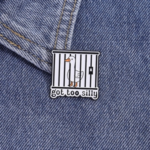 Detailed close-up of 'got too silly' goose enamel pin on blue denim fabric background
