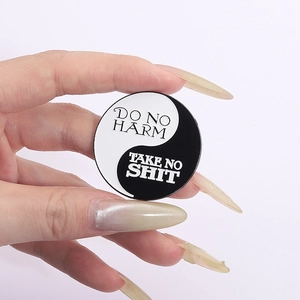 Yin Yang enamel pin with Do No Harm Take No Shit text held against white background