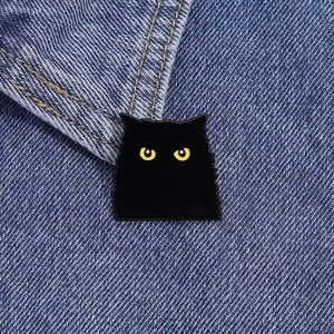 Détail macro du pin's émaillé chat noir avec yeux jaunes sur texture denim bleu
