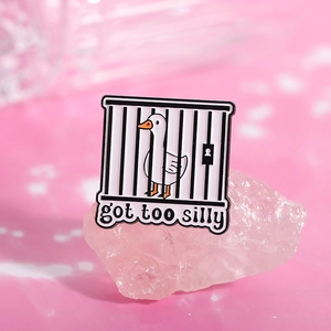 Macro view of a white enamel silly goose pin in a black cage with got too silly text