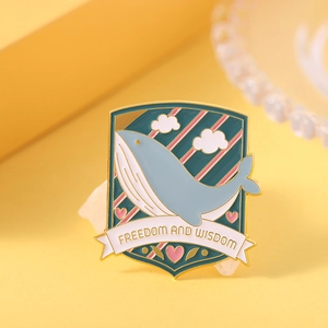 Close-up of whale enamel pin with Freedom and Wisdom text and metal lacquer finish