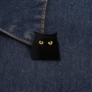 Détail macro d'un badge chat noir en émail avec yeux jaunes sur un tissu en jean