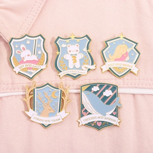 Close-up of five blue animal shield enamel pins with gold trim on pink denim