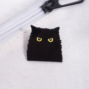 Détail d'un pin's chat noir émaillé aux yeux jaunes sur une toile blanche en coton